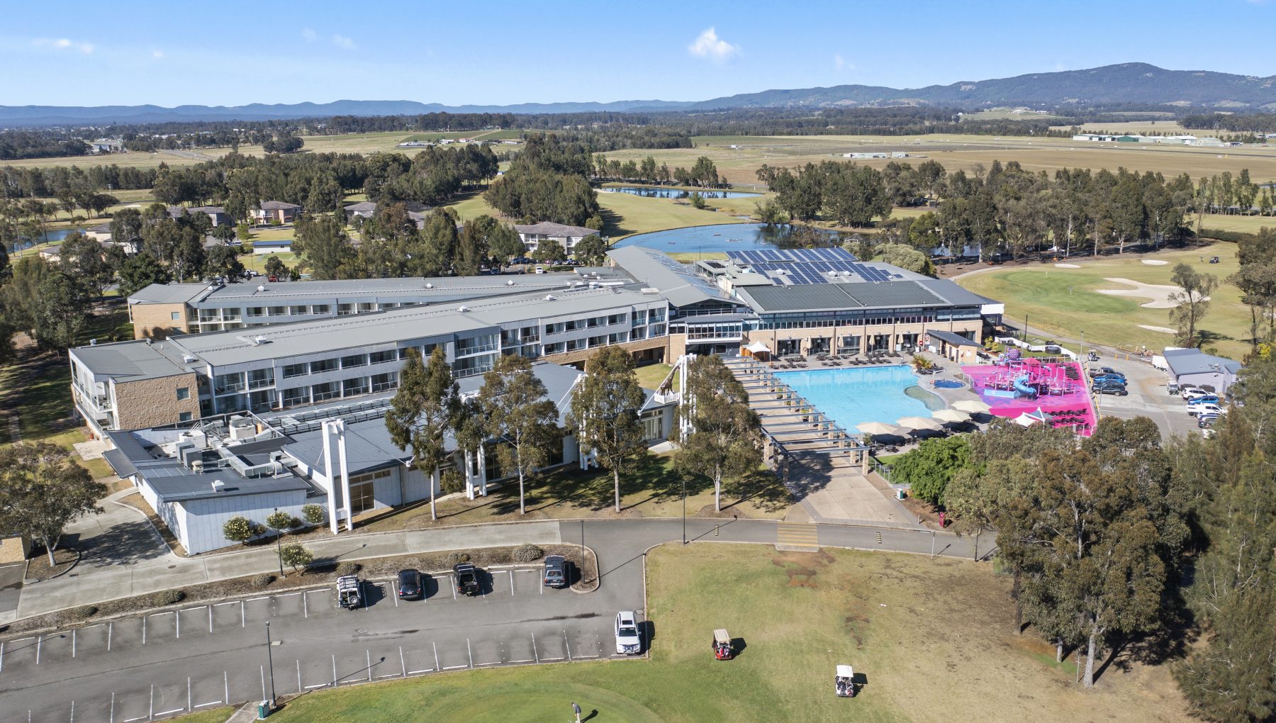Aerial view of a resort featuring a serene pool, vibrant water park, spacious car parks, hotel, lush golf course, and modern Conference Centre.
