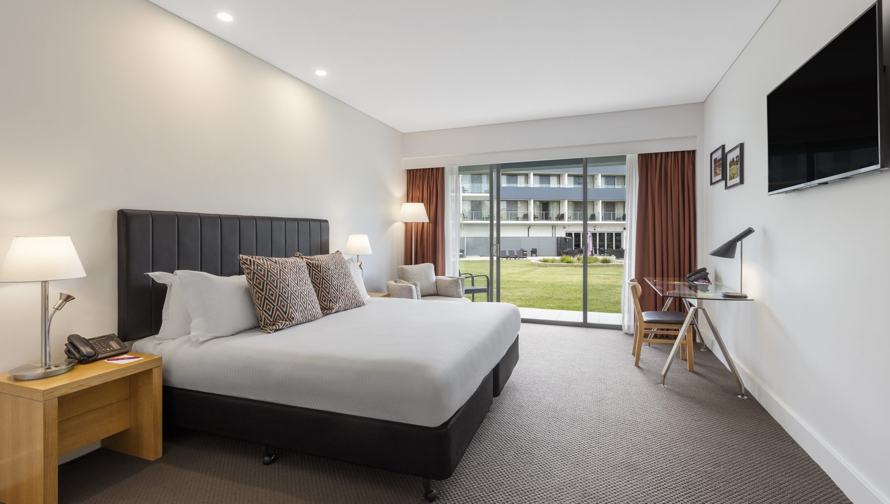 Image of an accessible room with a phone on the side table, warm lamps, and ample space around the bed for easy mobility.